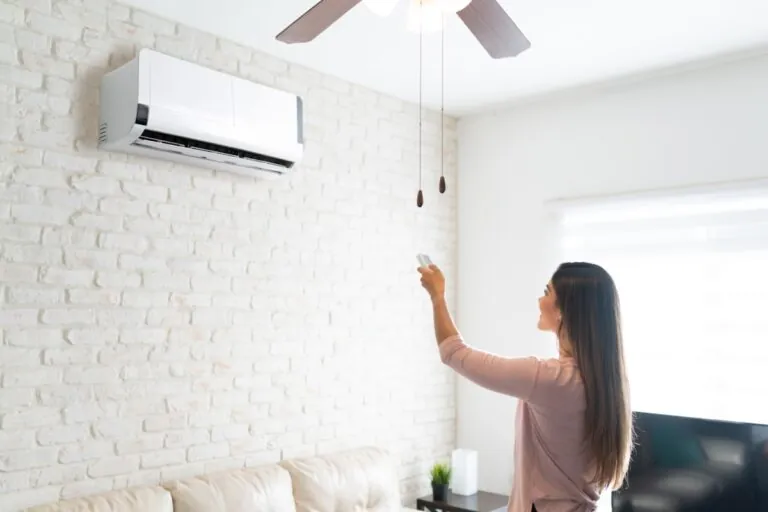 woman adjusting temperature of air conditioner using remote control in room at home