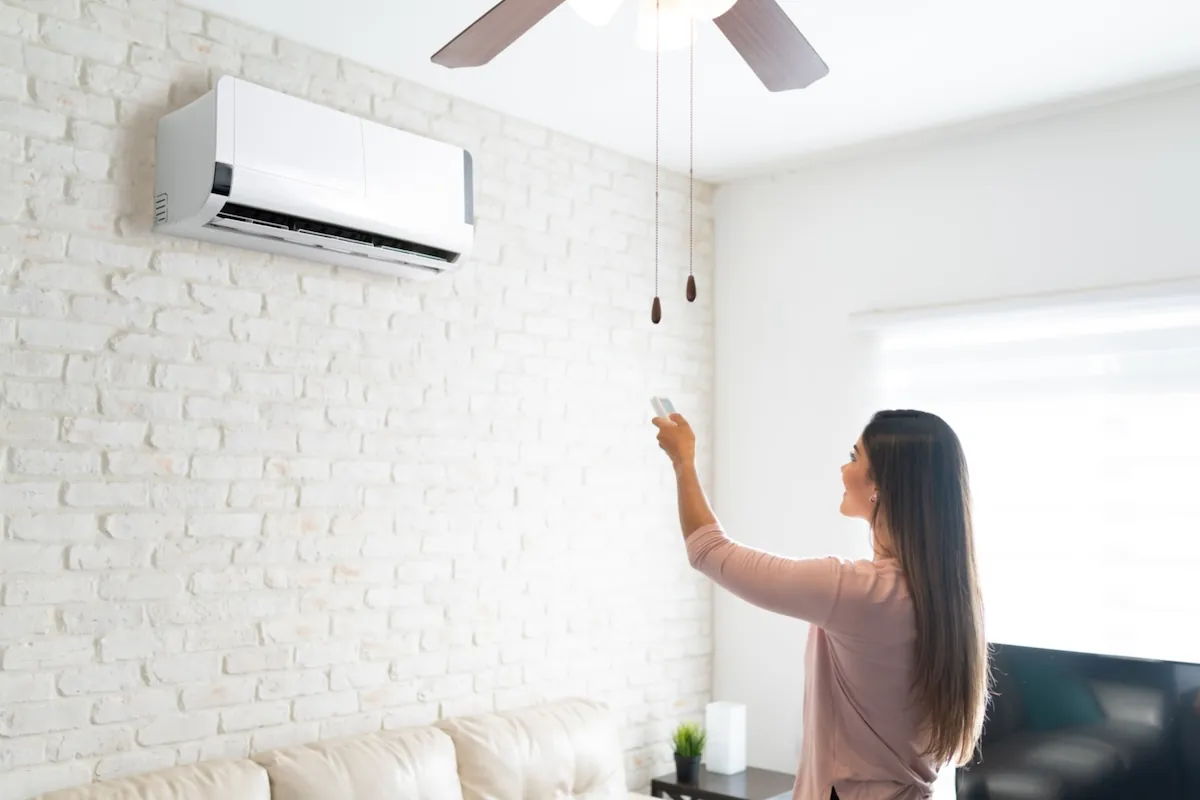 woman adjusting temperature of air conditioner using remote control in room at home