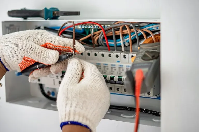 An electrical engineer is working on a home electrical control panel system and checking the current with a voltmeter.