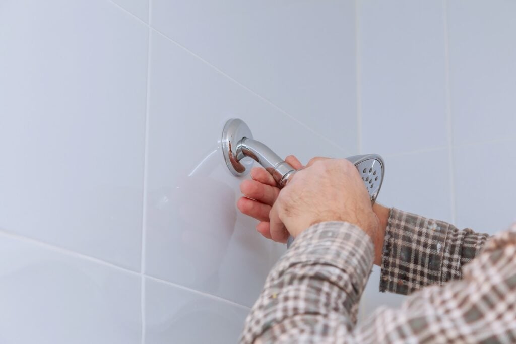 Plumber replacing in bathroom with height adjustable shower head shower holder is mounted on wall.
