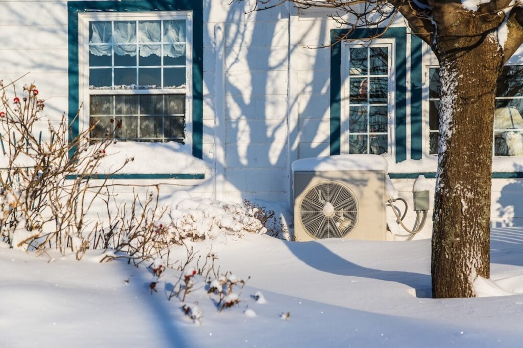 Heat pump unit on the side of a home in winter.
