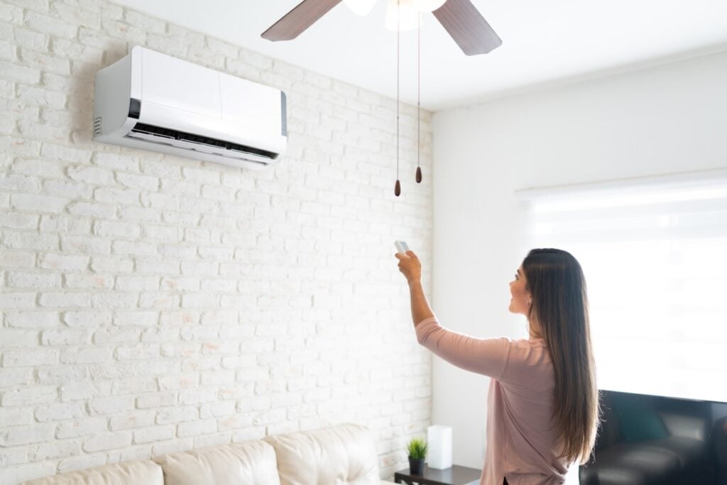woman adjusting temperature of air conditioner using remote control in room at home