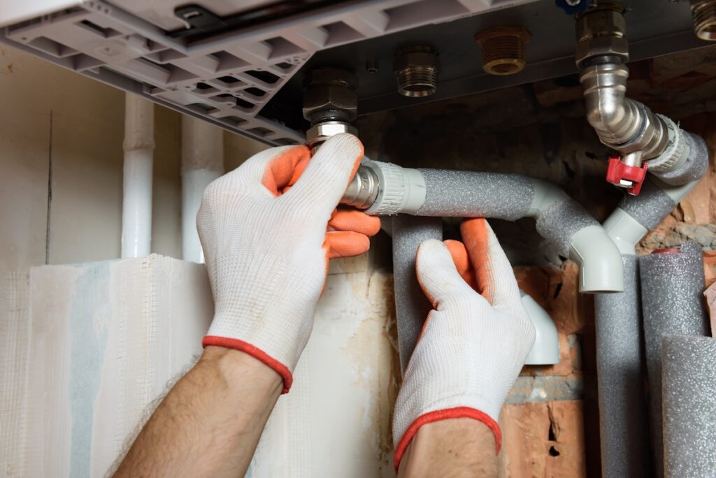 The worker is connecting the pipes to a domestic gas boiler.