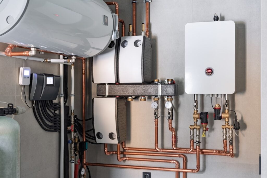 Heating system equipment in a boiler room of modern private house. Wall installation of electric boiler device, valves, pumps, cooper tubing, water heater, automatic controller in a single family home