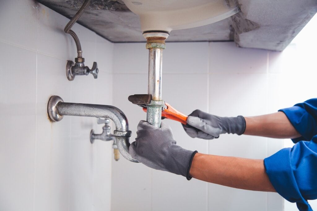 Technician plumber using a wrench to repair a water pipe under the sink