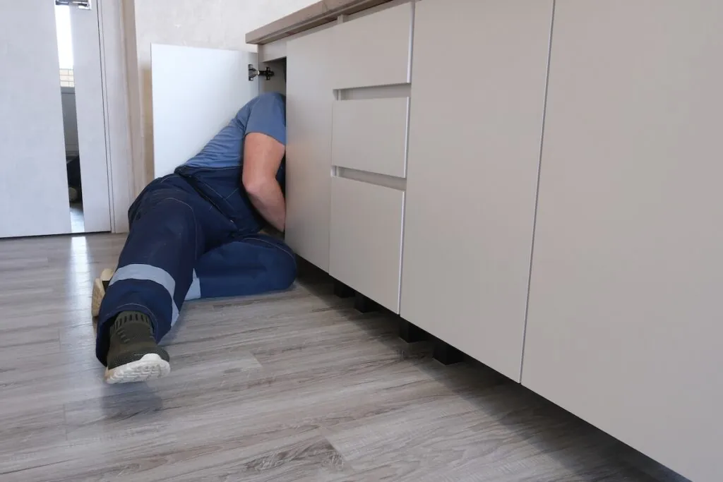 Man in overalls repairing pipes under a kitchen sink