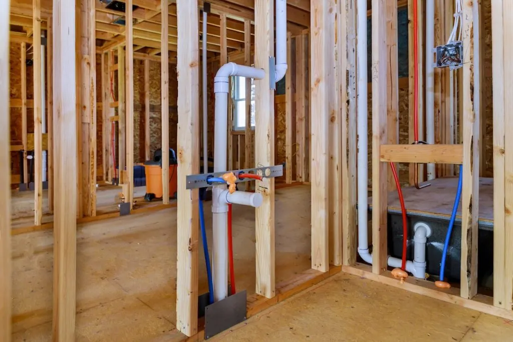 Applying pipe drain plumbing with hot red and cold blue pex pipe inside a house bathroom frame