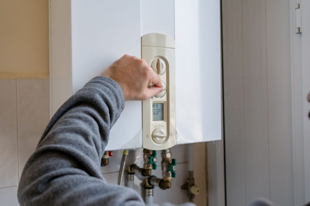 Man’s hand regulating the temperature dial of a wall-mounted boiler