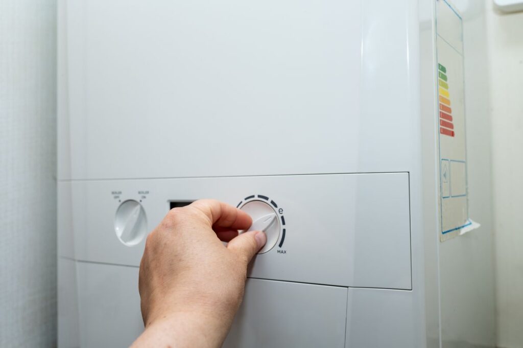 A hand turning the control knob on a household boiler to regulate heating