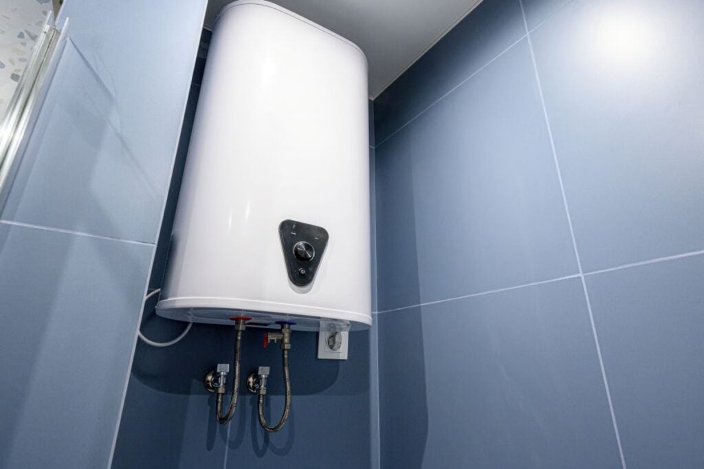 White electric water heater mounted on blue tiled wall in bathroom