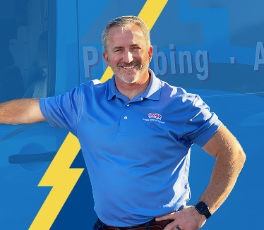 Smiling man in a blue polo with a company logo stands with one hand on his hip in front of a blue service van with a yellow lightning bolt graphic.